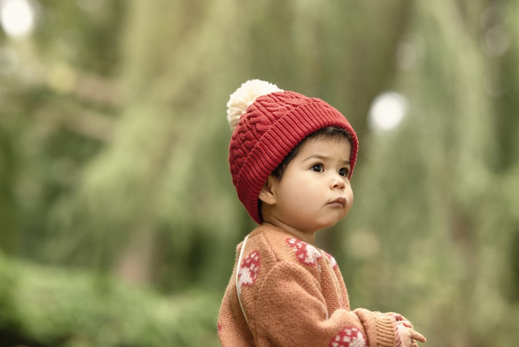 Bebé con gorro rojo sentado al pie de un árbol en el National Botanic Garden en Irlanda, junto a una ardilla en el césped.