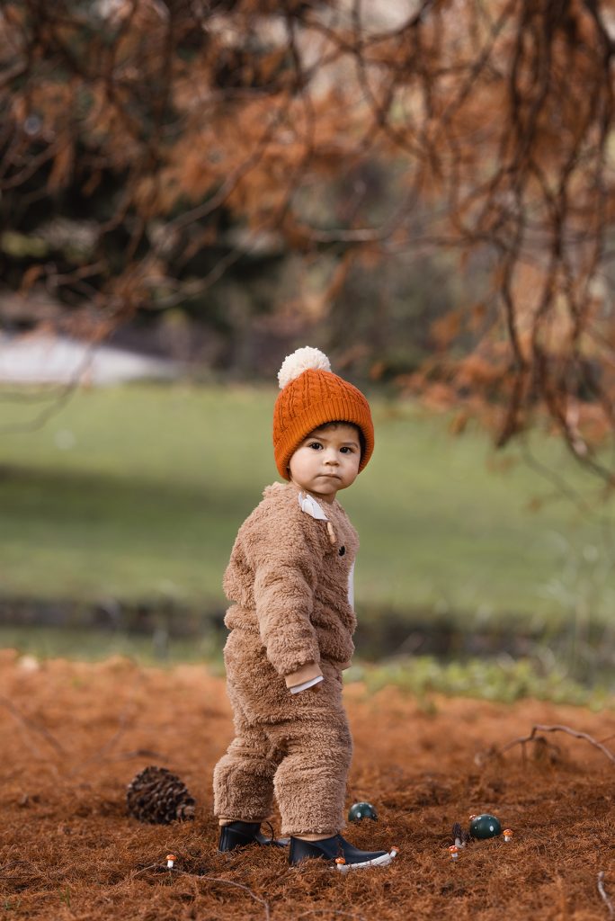Bebé con gorro rojo sentado al pie de un árbol en el National Botanic Garden en Irlanda, junto a una ardilla en el césped.